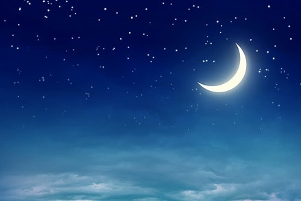 sleepy crescent moon in a starry night sky over low clouds