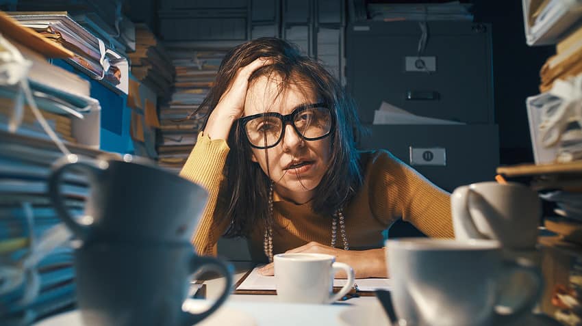 Stressed exhausted woman sitting at office desk and working overtime, she is overloaded with work with lack of sleep