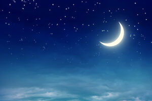 sleepy crescent moon in a starry night sky above soft clouds